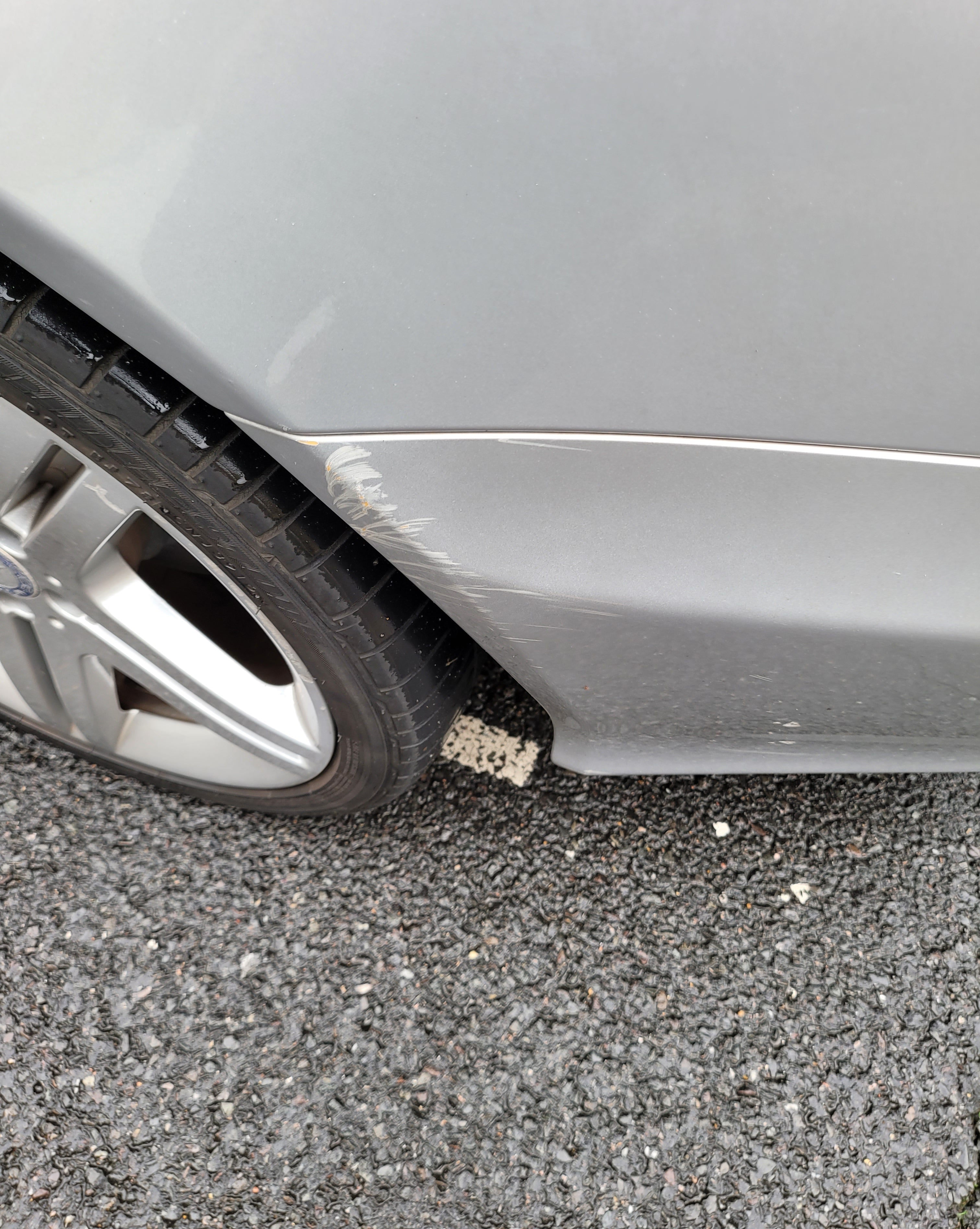 Car fender with a dent on a gray asphalt surface