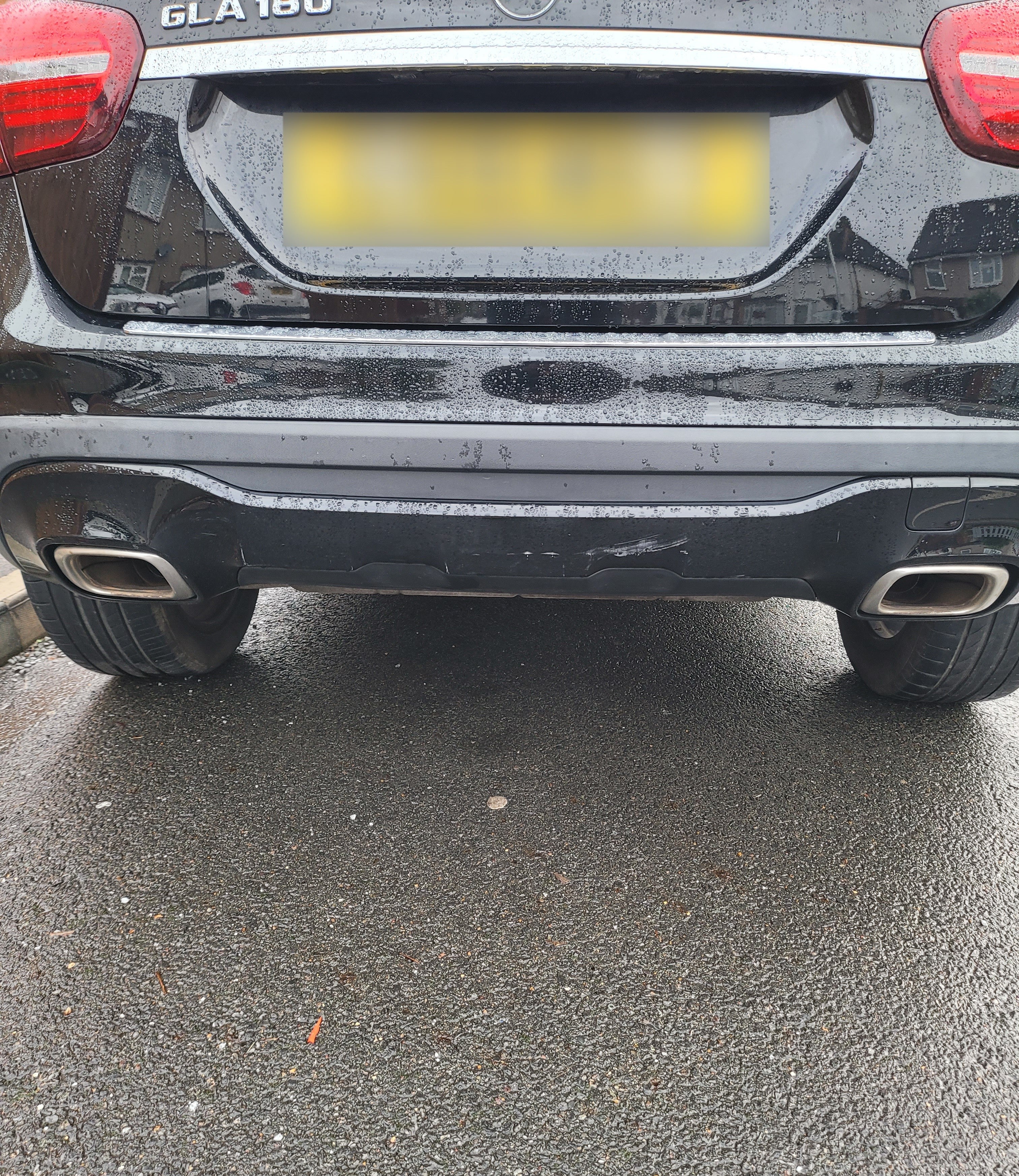 Back of a black car with a blurred license plate on a wet road.