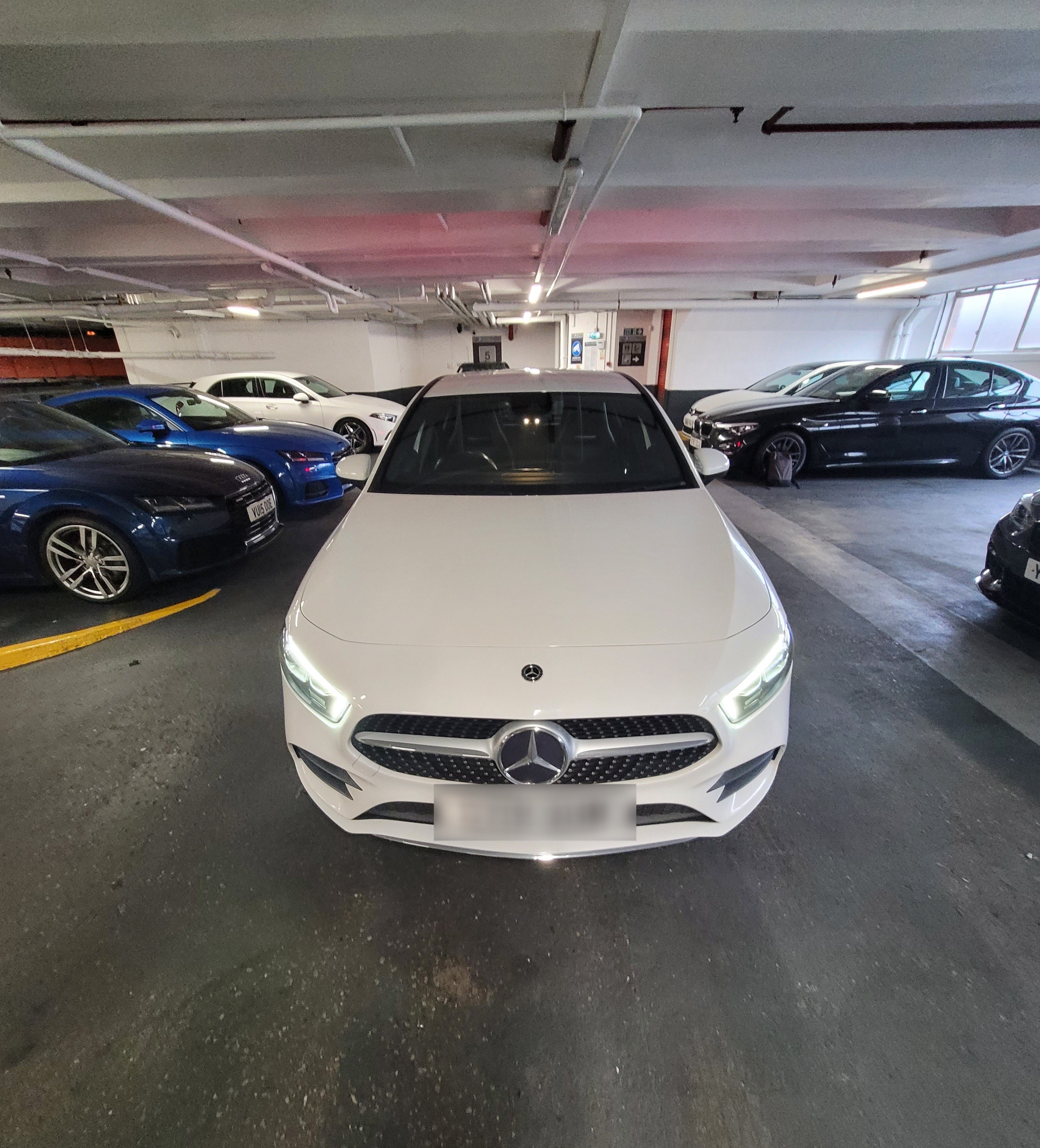 White Mercedes-Benz car in a parking garage with other cars around